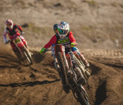 Piloto de Motocross en una pista de tierra con la rueda delantera levantada y otros dos pilotos detrás