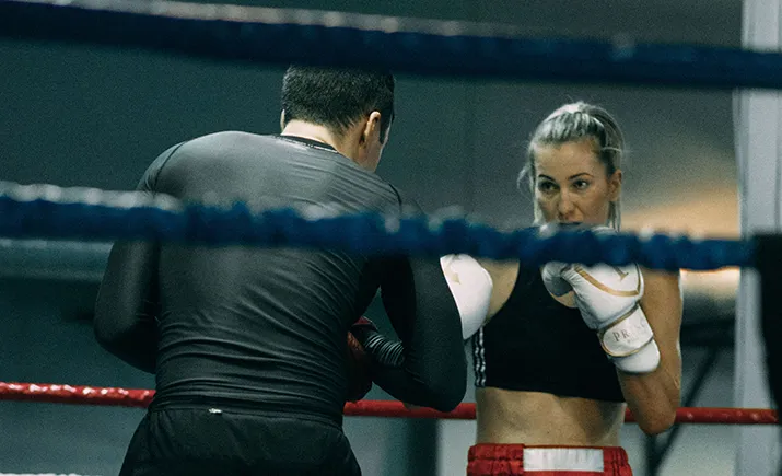 Una boxeadora entrena con su entrenador en el ring.