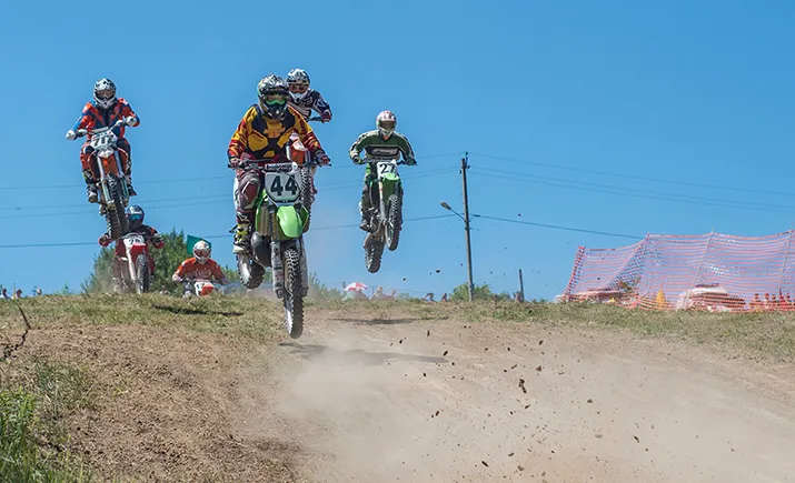 Six motocros riders coming down from a jump over a dirt ramp