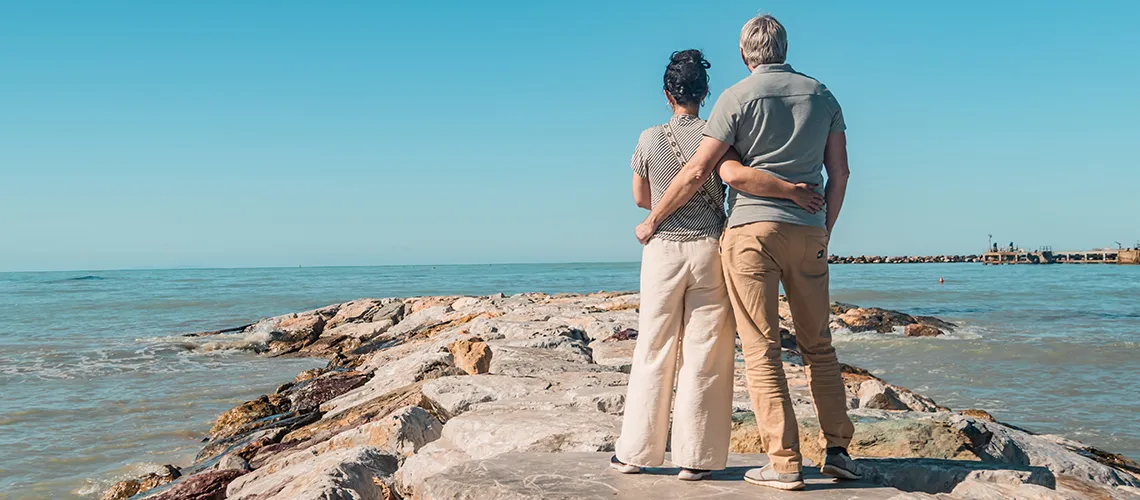 Couple hugging in front of a beach, looking out into the horizon